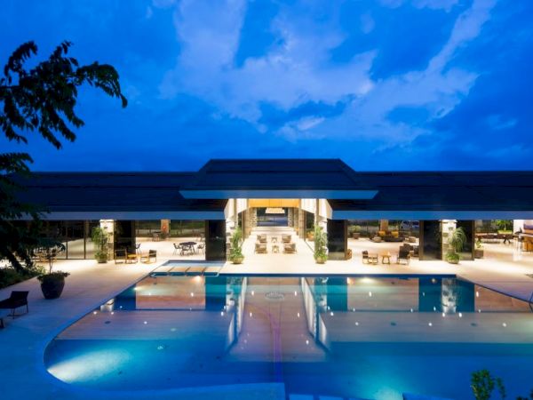 A luxurious building with a large, illuminated pool in front, surrounded by modern architecture under a twilight sky.