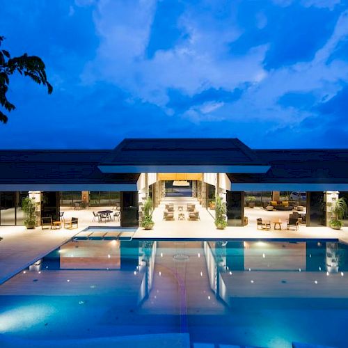 A luxurious pool area with elegant outdoor seating and warm lighting under a dramatic evening sky.