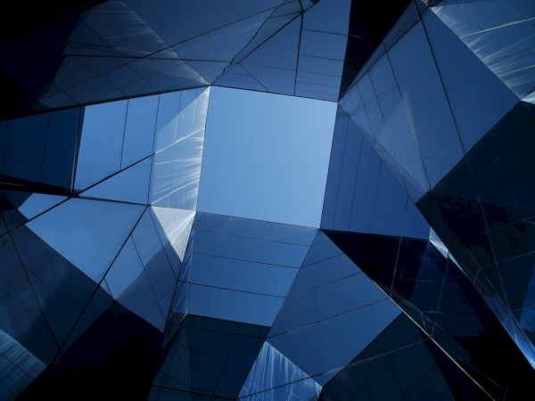 A view of a modern architectural structure with reflective glass surfaces, forming a geometric pattern against the sky.