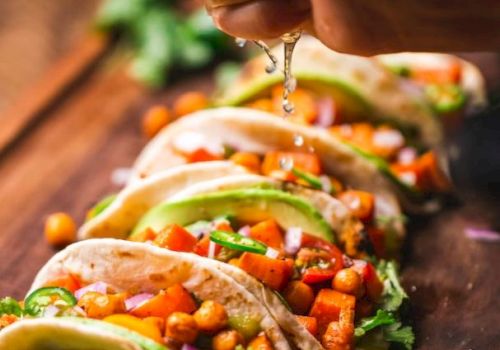 A person is squeezing lime juice over tacos filled with chickpeas, vegetables, and avocado slices on a wooden board.