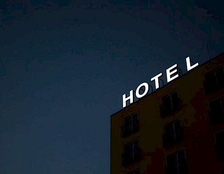 An exterior view of a building at night with a sign that says "HOTEL," with one letter not illuminated.