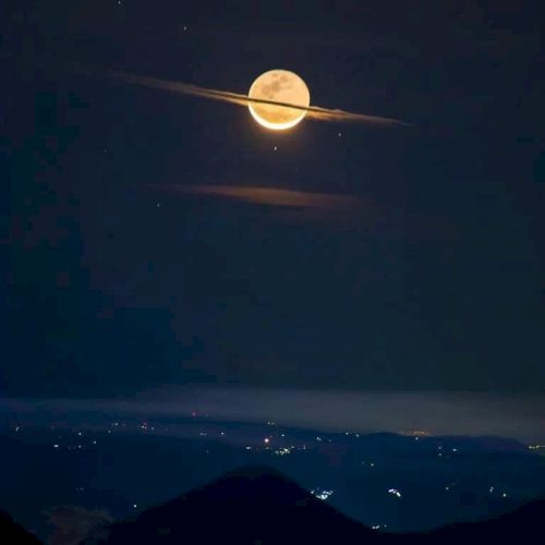 A full moon with clouds resembling Saturn's rings, set against a night sky over a landscape with distant lights.