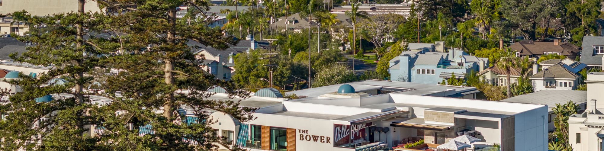 The image shows a modern building labeled "The Monsaraz," with a city skyline in the background and lush greenery around.