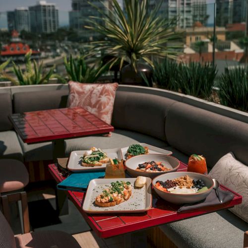 Outdoor dining setup with plates of food on a rooftop patio, city skyline in the background.