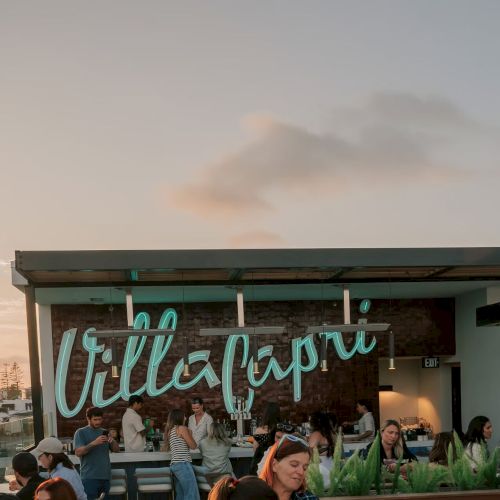 People are sitting at an outdoor dining area under a sign that reads "Villa Capri" at sunset.