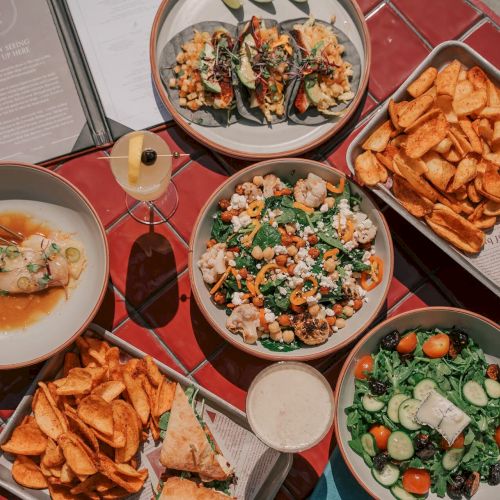 A table with tacos, potato wedges, sliders, salads, a sandwich, chips, drinks, and a menu, arranged on a round red table.