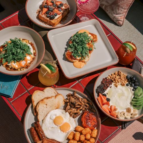 An assortment of brunch dishes including eggs, toast, salad, fruit bowls, and drinks on a red table.