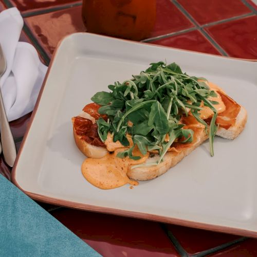 A dish with grilled scallops and greens on a plate, alongside a drink garnished with a lime and olives, resting on a red-tiled table.