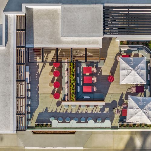 The image shows an aerial view of a rooftop patio with seating, tables, umbrellas, and planters, featuring a stylish, modern design.