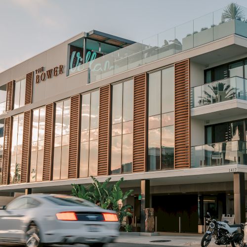 A modern building with large windows, a car passing by, and a parked motorcycle in the foreground.