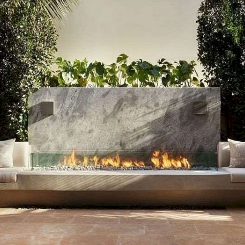 The image shows a modern outdoor seating area with a curved sofa, pillows, and a sleek fire feature in a landscaped setting.
