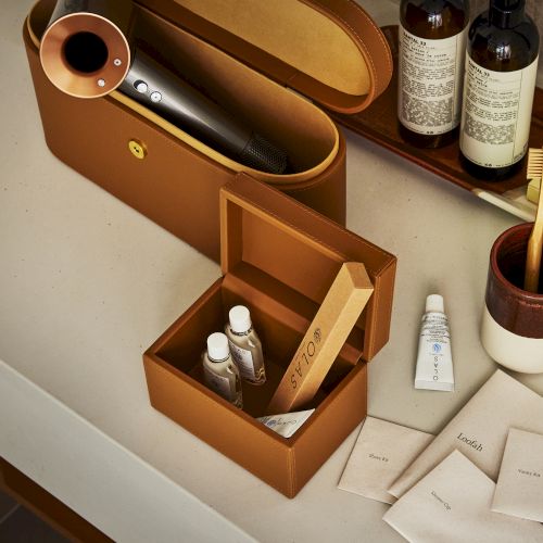 A wooden box with small drawers sits on a table, surrounded by bottles and a corkscrew, like a tiny vintage desk organizer.