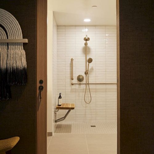 A doorway opens to a softly lit bathroom with a hanging towel, a towel rack, a small chair, and a chandelier reflected in the mirror.