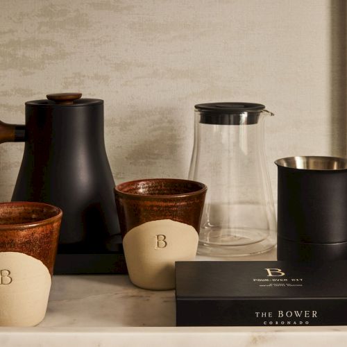 A row of bottles and jars on a kitchen counter, with a small potted plant and a ceramic mug, all in a warm, cozy setting.