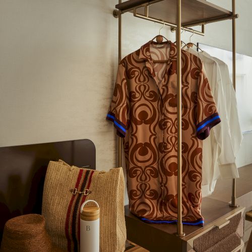 A small clothing rack with a colorful patterned shirt, a beige bag, and a brown couch in a cozy corner.