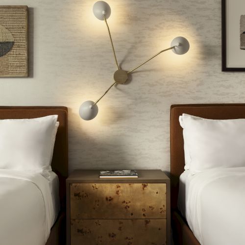 Two single beds with a shared nightstand between them, modern wall lamps, and framed art on a neutral-toned wall.