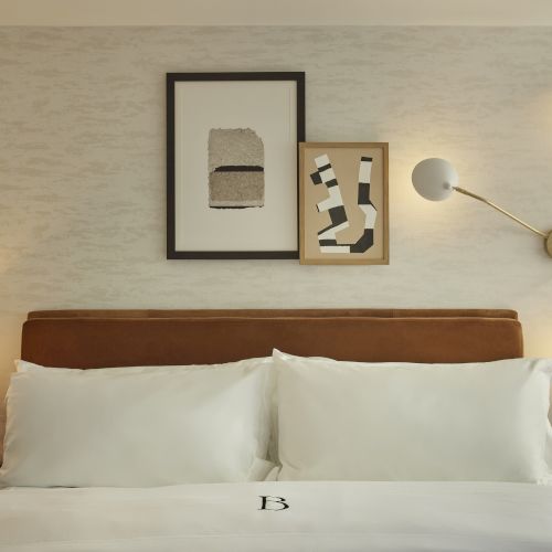 A cozy hotel room with a king bed, soft lighting, framed art, nightstands, and a lamp; minimalist and inviting.
