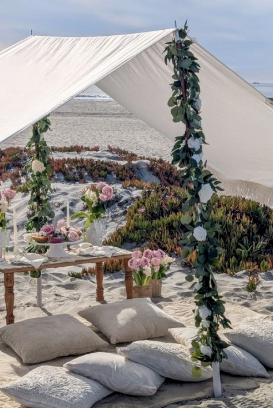 A beach setup with a canopy, table, cushions, flowers, and a "Happy Valentine's" chalkboard.