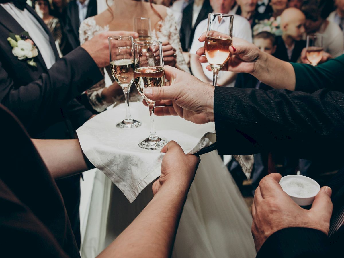 People are gathered, holding glasses for a toast, possibly at a celebration or wedding, with champagne being served on a tray.