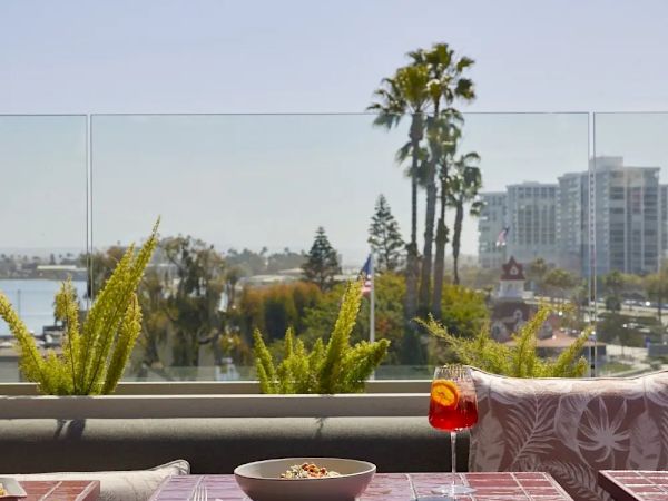 Open-air dining setup with a shaded table, plants, and city view with palm trees and buildings in the background.