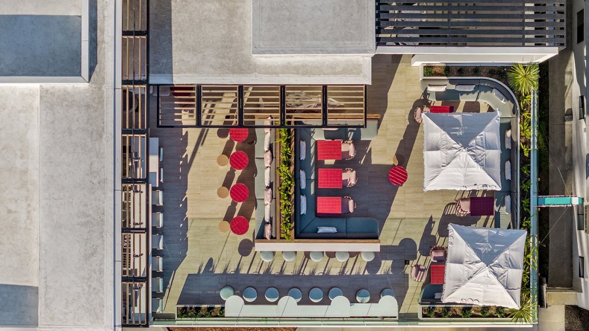 An aerial view of a stylish outdoor patio with seating, umbrellas, and red accents, situated on a rooftop deck in an urban setting.