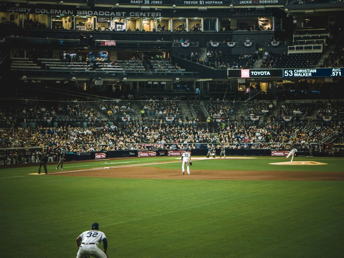 The image shows a baseball game in progress at a stadium, with players on the field and spectators in the stands under the lights.