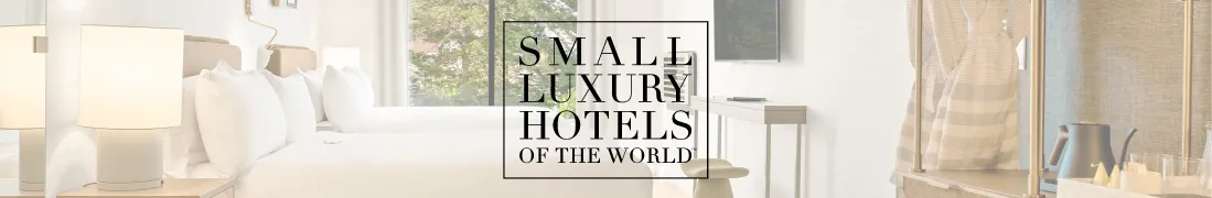 A stylish hotel room with a bright, airy lounge and modern amenities, featuring plush white bedding and sleek decor. Small Luxury Hotels of the World branding centered on the image.
