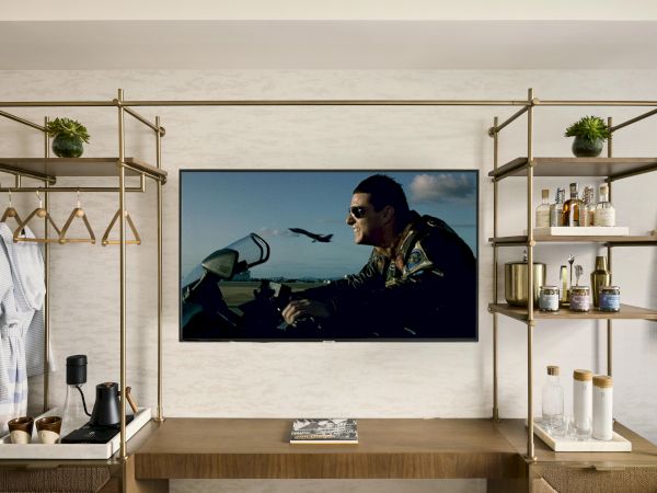 A stylish living area with a wall-mounted TV, open wooden shelving on both sides, and assorted decor and accessories. Top it at 140 characters, always ending the sentence.
