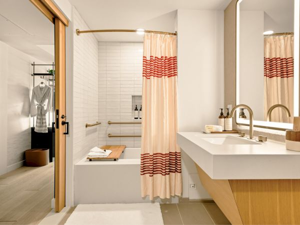 A modern bathroom with a bathtub behind a pink striped shower curtain, a double sink vanity, large mirrors, and warm wood accents.