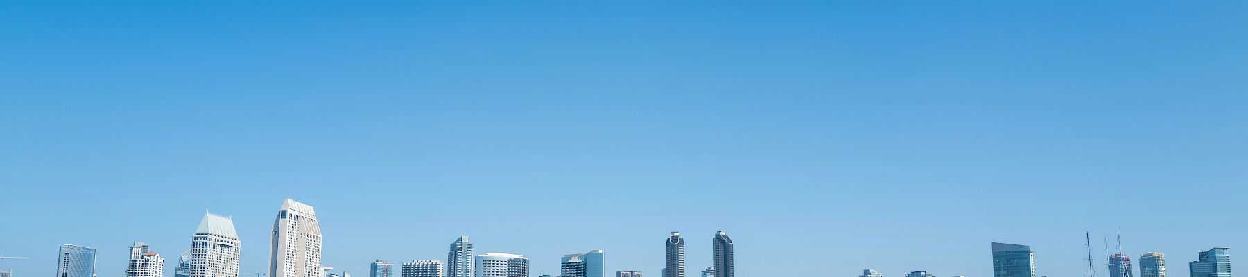 A sunny waterfront skyline with tall buildings, a dock, and small boats on the water.