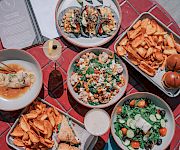 A table spread with salad bowls, loaded fries, a burger, and other mixed dishes, ready to share and dig in.