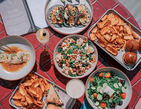 A table spread with salad bowls, loaded fries, a burger, and other mixed dishes, ready to share and dig in.