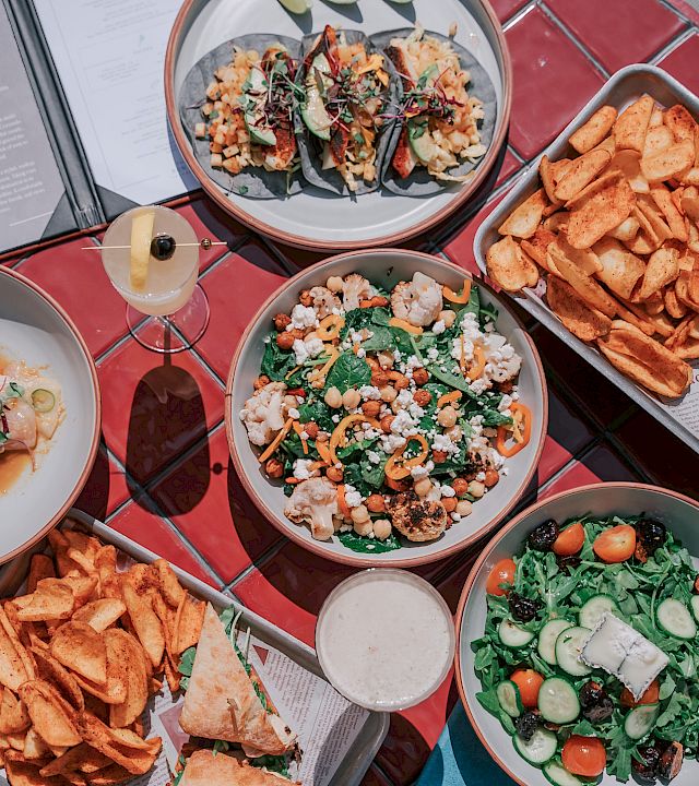 A table spread with salad bowls, loaded fries, a burger, and other mixed dishes, ready to share and dig in.