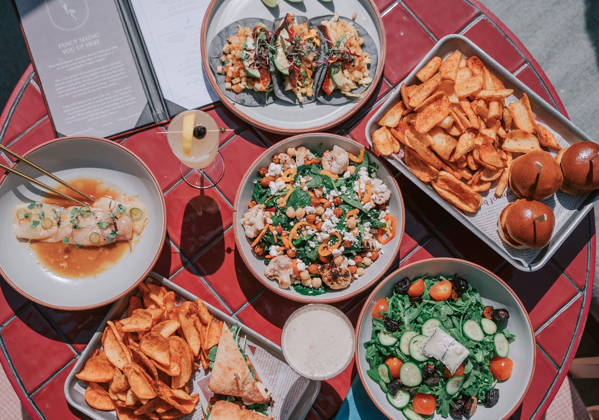 A table spread with salad bowls, loaded fries, a burger, and other mixed dishes, ready to share and dig in.