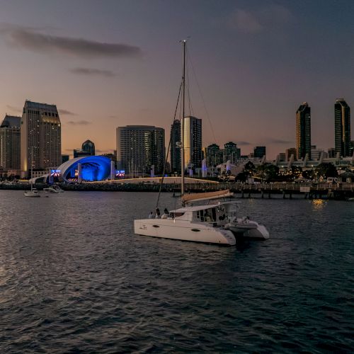 A marina with a white yacht in the foreground and a lit city skyline at dusk, captured from the water.