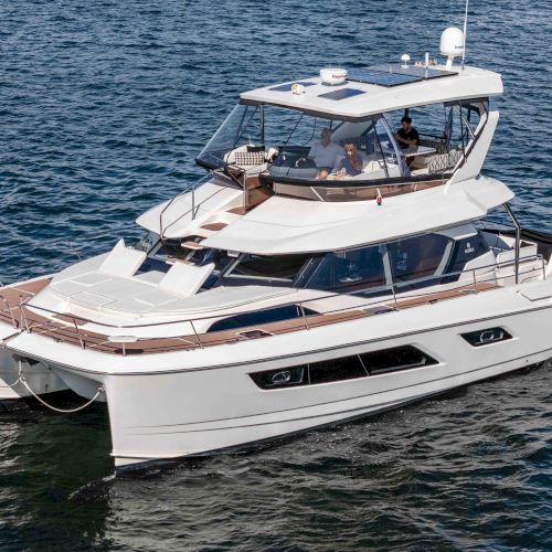 A luxury motor yacht cruising on open water with passengers aboard and radar/solar gear on the upper deck.