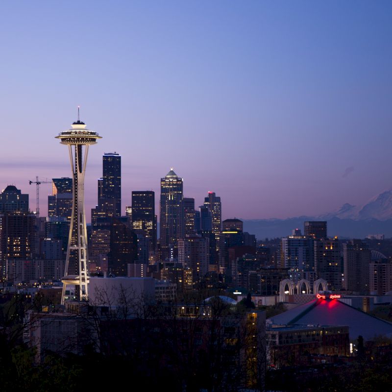 Seattle skyline at dusk featuring the Space Needle with Mount Rainier in the background under a clear, colorful sky.