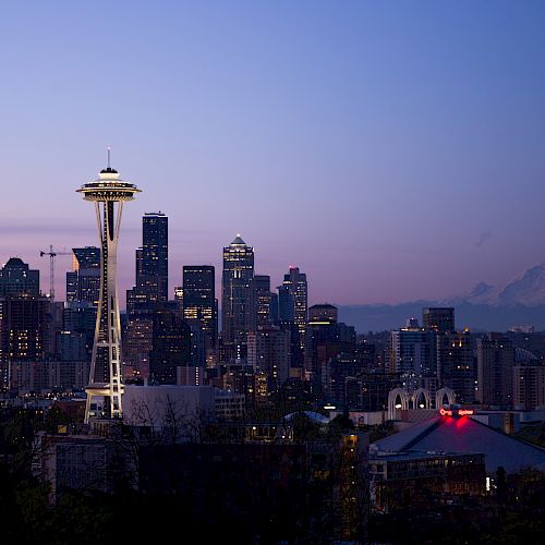 The image shows the Seattle skyline at dusk, featuring the Space Needle and Mount Rainier in the background against a twilight sky.