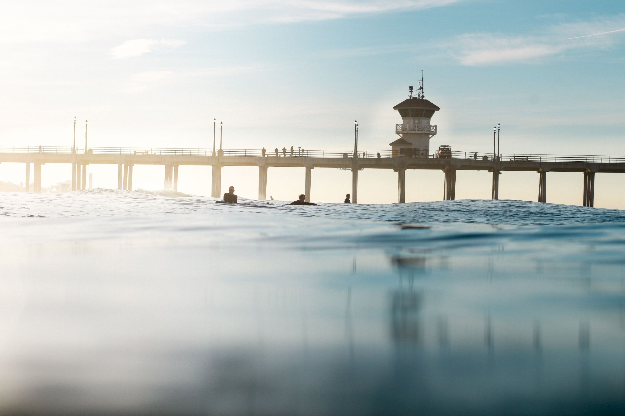 The image shows a serene view of the ocean with a pier extending into the water, silhouetted figures, and a hazy sky at sunrise or sunset.